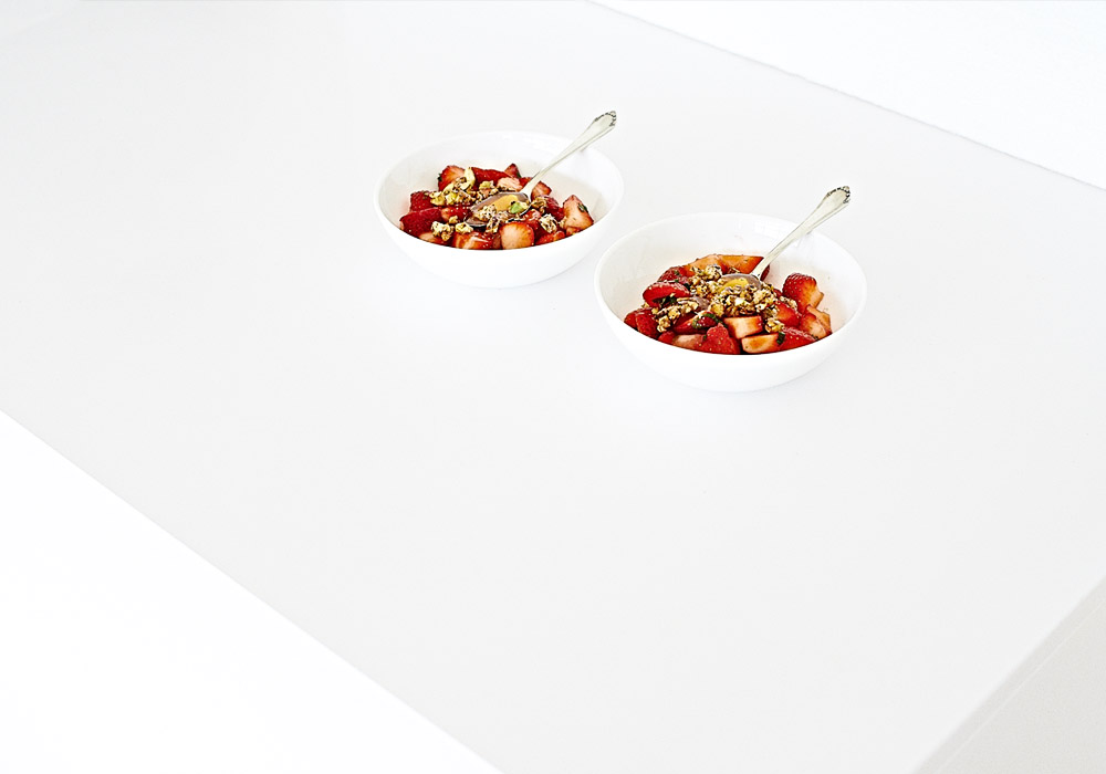 Moderne Food-Fotografie leckeres Dessert mit frischen Erdbeeren und karamellisierten Nüssen in weißer Küche mit viel Freiraum